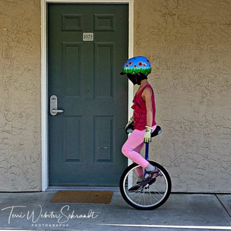 Girl on unicyle rolls by motel door