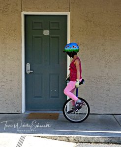 Girl on unicyle rolls by motel door